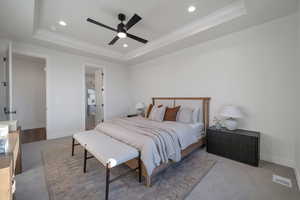 Bedroom with a tray ceiling, ceiling fan, light colored carpet, and ensuite bathroom