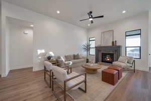 Living room with a fireplace, wood-type flooring, and ceiling fan