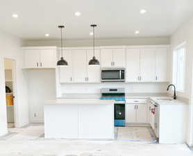 Kitchen featuring stainless steel appliances, sink, decorative light fixtures, white cabinets, and a center island