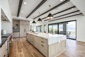 Kitchen with beam ceiling, a large island with sink, pendant lighting, light brown cabinetry, and high end range