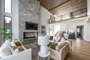 Living room featuring a stone fireplace, high vaulted ceiling, wood ceiling, and hardwood / wood-style flooring