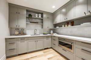 Kitchen with gray cabinetry, stainless steel oven, sink, decorative backsplash, and light hardwood / wood-style floors