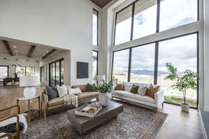 Living room with wood-type flooring, a towering ceiling, a wealth of natural light, and beam ceiling