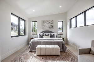 Carpeted bedroom with vaulted ceiling and multiple windows