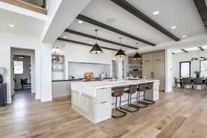 Kitchen featuring beamed ceiling, decorative light fixtures, light hardwood / wood-style floors, and a large island with sink