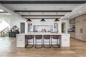 Kitchen with beamed ceiling, pendant lighting, light hardwood / wood-style flooring, and a large island with sink