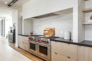 Kitchen with light brown cabinetry, backsplash, dark stone counters, light hardwood / wood-style flooring, and double oven range