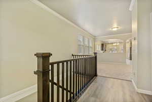 Hallway with light wood-type flooring, crown molding, and a notable chandelier