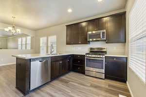 Kitchen with sink, light hardwood / wood-style flooring, appliances with stainless steel finishes, decorative light fixtures, and kitchen peninsula