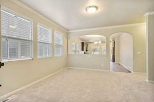 Carpeted spare room with an inviting chandelier, crown molding, and a healthy amount of sunlight