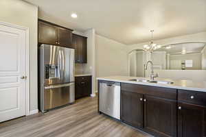 Kitchen featuring sink, light wood-type flooring, decorative light fixtures, dark brown cabinetry, and stainless steel appliances