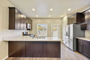 Kitchen with kitchen peninsula, appliances with stainless steel finishes, light wood-type flooring, and sink