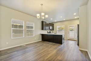 Kitchen featuring dark wood-type flooring, kitchen peninsula, appliances with stainless steel finishes, dark brown cabinetry, and a chandelier