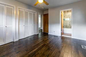 Main floorMaster bedroom featuring ensuite bath, ceiling fan, dark wood-type flooring, and two closets