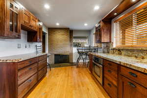 Kitchen with a fireplace, light stone countertops, stainless steel oven, and light wood flooring