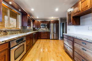 Kitchen featuring light stone countertops, sink, appliances with stainless steel finishes, and light hardwood / wood-style flooring