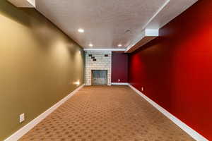 Basement family room featuring unfinished fireplace, carpet flooring and a textured ceiling