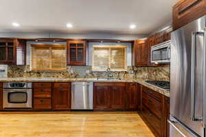 Kitchen with backsplash, sink, appliances with stainless steel finishes, and light hardwood flooring