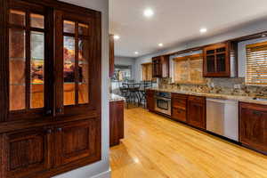 Kitchen with backsplash, light stone counters, light hardwood flooring, and appliances with stainless steel finishes