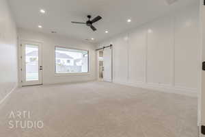 Interior space with ceiling fan, a barn door, light carpet, and access to outside