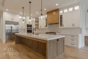 Kitchen with a center island with sink, built in appliances, white cabinetry, and tasteful backsplash