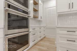 Kitchen featuring white cabinets, light hardwood / wood-style floors, stainless steel double oven, and backsplash