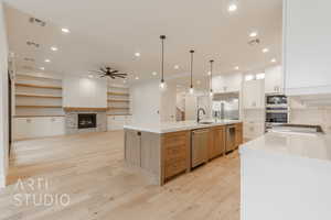 Kitchen featuring ceiling fan, a large island with sink, built in appliances, pendant lighting, and white cabinetry