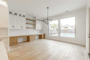 Interior space with white cabinets, light hardwood / wood-style floors, built in desk, and tasteful backsplash