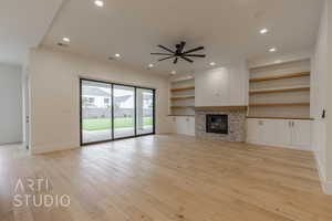 Unfurnished living room featuring ceiling fan, light hardwood / wood-style floors, and a stone fireplace