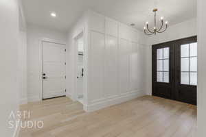 Foyer with french doors, a notable chandelier, and light wood-type flooring