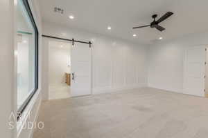 Spare room featuring a barn door, light carpet, and ceiling fan