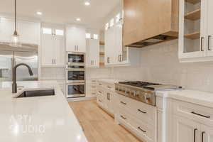 Kitchen with light wood-type flooring, tasteful backsplash, sink, pendant lighting, and built in appliances