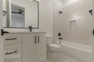 Full bathroom with ceiling fan, vanity, tiled shower / bath combo, and toilet