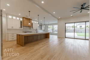 Kitchen with decorative backsplash, light wood-type flooring, sink, white cabinets, and a large island