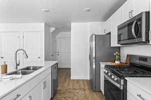 Kitchen featuring hardwood / wood-style floors, sink, a textured ceiling, appliances with stainless steel finishes, and white cabinetry