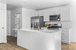 Kitchen with a textured ceiling, stainless steel appliances, a kitchen island with sink, wood-type flooring, and white cabinets