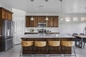 Kitchen featuring sink, appliances with stainless steel finishes, a kitchen breakfast bar, pendant lighting, and a kitchen island with sink