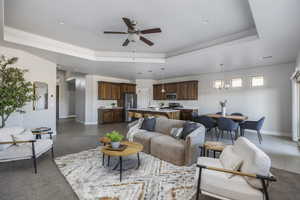 Tiled living room with a raised ceiling and ceiling fan with notable chandelier