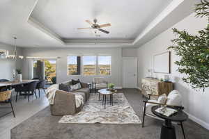 Tiled living room with a raised ceiling and ceiling fan with notable chandelier