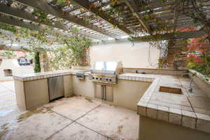 View of patio featuring a pergola, exterior kitchen, sink, and grilling area