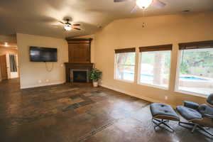 Unfurnished living room with ceiling fan, a large fireplace, and vaulted ceiling