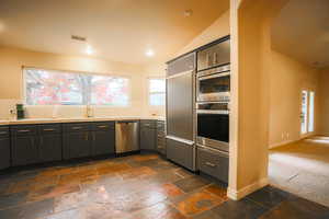 Kitchen with dark colored carpet, built in appliances, vaulted ceiling, and sink