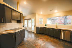 Kitchen with tile countertops, dishwasher, black electric stovetop, sink, and decorative backsplash