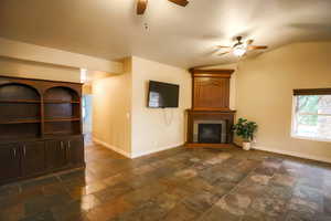 Unfurnished living room featuring a large fireplace, ceiling fan, and lofted ceiling