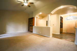 Unfurnished living room with carpet, ornate columns, built in shelves, ceiling fan with notable chandelier, and lofted ceiling