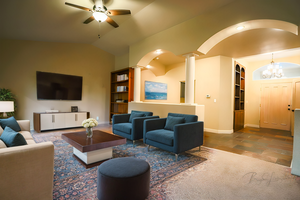 Living room with built in shelves, ceiling fan with notable chandelier, ornate columns, and vaulted ceiling