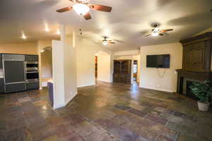 Unfurnished living room with a large fireplace, ceiling fan, and lofted ceiling