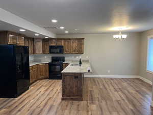 Kitchen featuring kitchen peninsula, an inviting chandelier, light hardwood / wood-style flooring, and black appliances