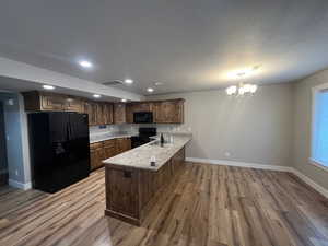 Kitchen featuring an inviting chandelier, black appliances, sink, light hardwood / wood-style floors, and kitchen peninsula