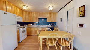 Kitchen featuring light brown cabinetry, light wood-type flooring, backsplash, white appliances, and sink